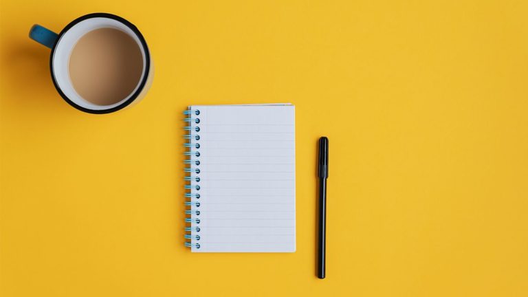 记事本和黑色钢笔与咖啡杯与奶油在黄色的背景